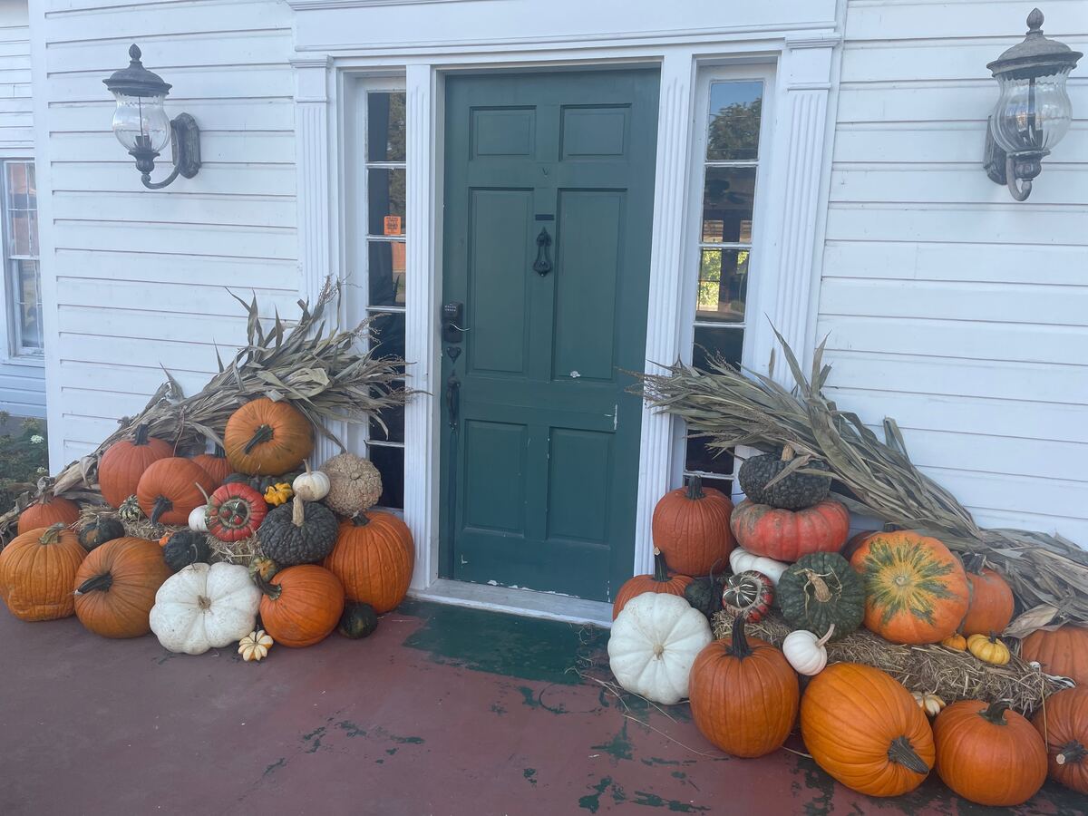 A porch entry framed with pumpkins and autumn foliage